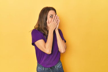 Güzel yetişkin bir kadının portresi parmaklarının arasından korkmuş ve gergin bir şekilde göz kırpıyor..