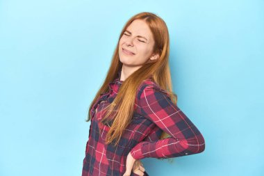 Mavi arka plandaki kızıl saçlı genç kadın sırt ağrısı çekiyor..