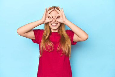 Mavi arka plandaki kızıl saçlı genç kadın gözlerinde sorun olmadığını gösteriyor.