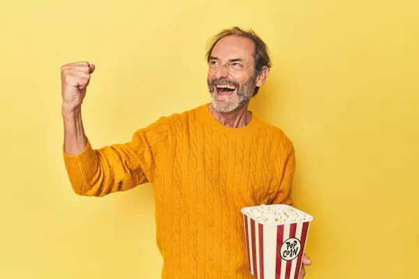 Człowiek Korzystających Popcorn Żółtym Studio Podnosząc Pięść Zwycięstwie Koncepcja Zwycięzcy — Zdjęcie stockowe