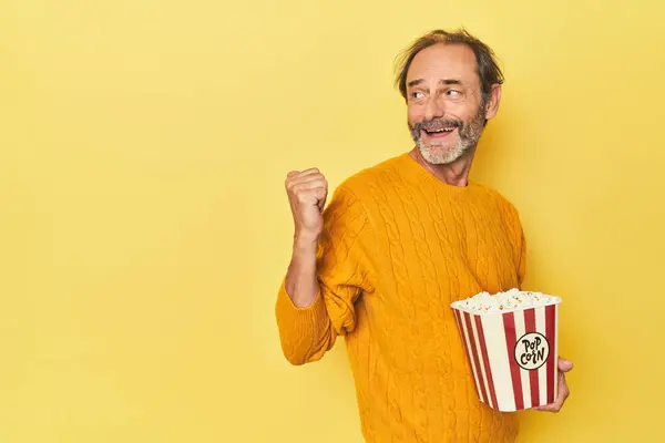 Man Enjoying Popcorn Yellow Studio Points Thumb Finger Away Laughing — Stock Photo, Image
