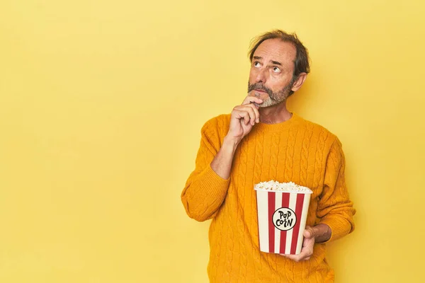 Man Enjoying Popcorn Yellow Studio Looking Sideways Doubtful Skeptical Expression — Stock Photo, Image