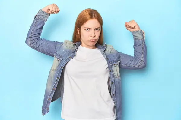 红头发的年轻女子 蓝色背景 手臂有力的姿势 女性力量的象征 — 图库照片