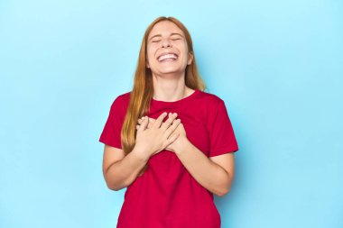 Mavi arka plandaki kızıl saçlı genç kadın gülüyor ellerini yüreğine koyuyor, mutluluk kavramını koruyor..