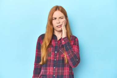 Mavi arka planda kızıl saçlı genç bir kadın güçlü bir diş ağrısı ve azı dişi ağrısı var..