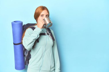 Dağcı kızıl saçlı, mavi stüdyoda kamp bardağından yudumluyor.