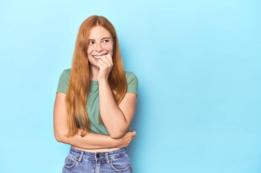 Mavi arka plandaki kızıl saçlı genç kadın rahatlamış fotokopi odasına bakan bir şey düşünüyor..