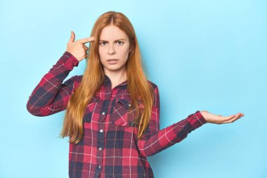 Mavi arka plandaki kızıl saçlı genç kadın elinde bir ürün tutuyor ve.