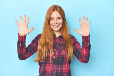 Mavi arka plandaki kızıl saçlı genç kadın on numarayı elleriyle gösteriyor..