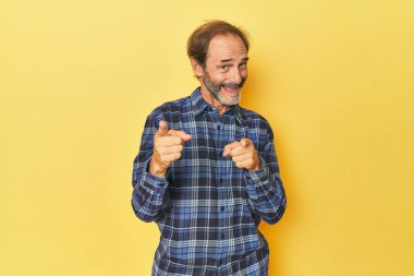 Sarı stüdyodaki orta yaşlı adam parmaklarıyla ön tarafı işaret ediyor..