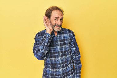 Sarı stüdyoda orta yaşlı beyaz bir adam bir dedikoduyu dinlemeye çalışıyor..