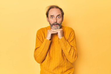 Sarı stüdyoda orta yaşlı beyaz bir adam şans için dua ediyor, şaşırmış ve ağzını açıyor..