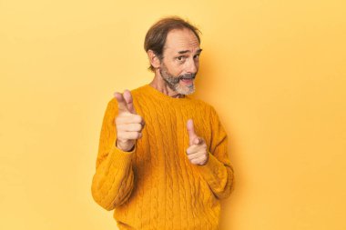 Sarı stüdyodaki orta yaşlı adam parmaklarıyla ön tarafı işaret ediyor..