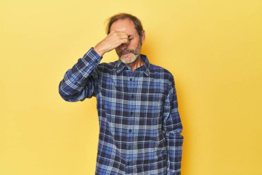 Sarı stüdyodaki orta yaşlı adamın başı ağrıyor, yüzüne dokunuyor..