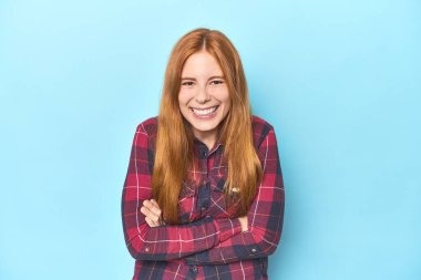 Mavi arka plandaki kızıl saçlı genç kadın gülüyor ve eğleniyor..