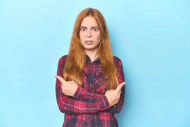 Mavi arka plandaki kızıl saçlı genç kadın iki seçenek arasında seçim yapmaya çalışıyor..