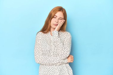 Mavi arka planda, sıkılmış, yorgun ve dinlenmeye ihtiyacı olan kızıl saçlı genç bir kadın..