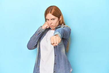 Mavi arka plandaki kızıl saçlı genç kadın bir tartışma yüzünden yumruk, öfke, kavga, boks atıyor..