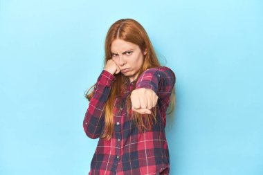 Mavi arka plandaki kızıl saçlı genç kadın bir tartışma yüzünden yumruk, öfke, kavga, boks atıyor..