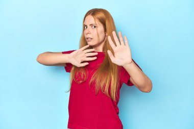 Mavi arka plandaki kızıl saçlı genç kadın yakın bir tehlikeden dolayı şoka uğruyor.