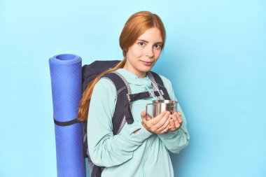 Dağcı kızıl saçlı, mavi stüdyoda kamp bardağından yudumluyor.