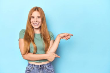 Mavi arka plandaki kızıl saçlı genç kadın işaret parmağıyla işaret ettiği için heyecanlı..