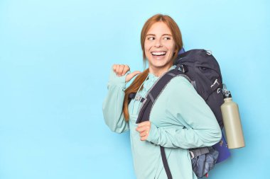 Stüdyo noktalarında sırt çantası ve paspası olan kızıl saçlı gezgin başparmağıyla gülüyor ve kaygısız..