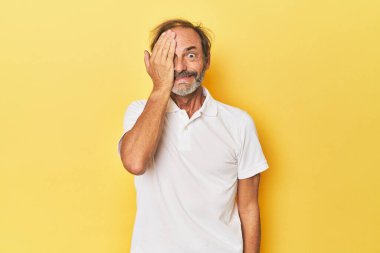 Sarı stüdyoda orta yaşlı bir adam yüzünün yarısını palmiye ile örterek eğleniyor..