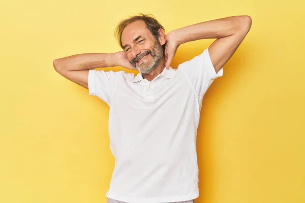 Caucasian middle-aged man in yellow studio stretching arms, relaxed position.