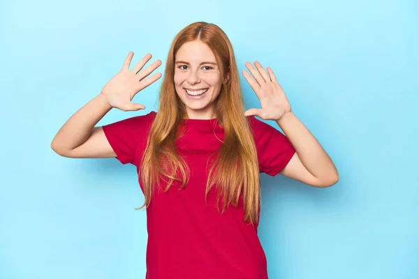 手でナンバー10を示す青い背景の赤毛の若い女性 — ストック写真