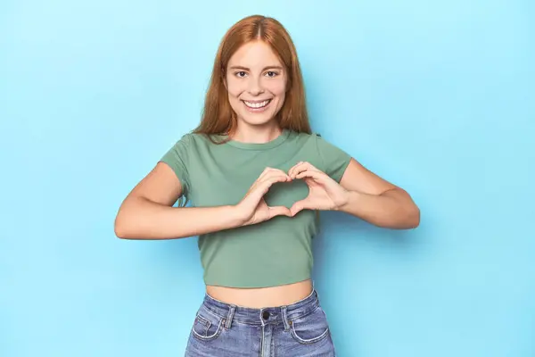 Roodharige Jonge Vrouw Blauwe Achtergrond Glimlachen Tonen Een Hart Vorm — Stockfoto