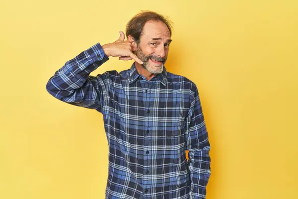 Sarı stüdyodaki orta yaşlı beyaz adam cep telefonu hareketini parmaklarıyla gösteriyor..