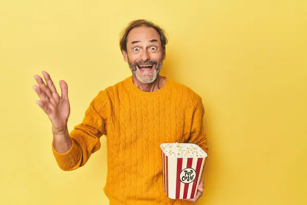 Man Enjoying Popcorn Yellow Studio Receiving Pleasant Surprise Excited Raising — Stock Photo, Image