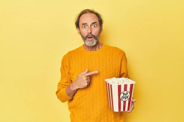 Man Enjoying Popcorn Yellow Studio Pointing Side — Stock Photo, Image