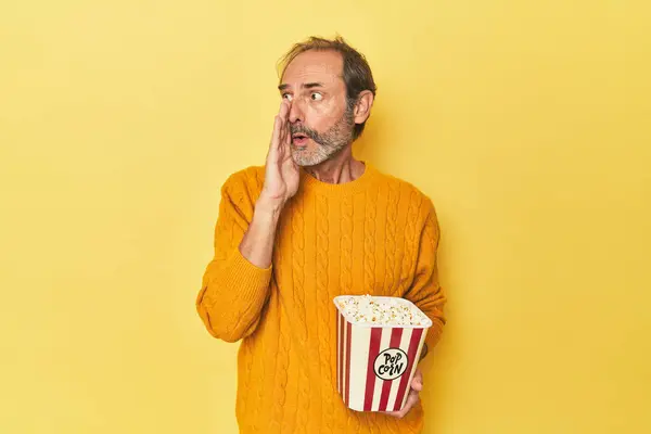 Mężczyzna Cieszący Się Popcornem Żółtym Studiu Mówi Sekretne Gorące Wiadomości — Zdjęcie stockowe