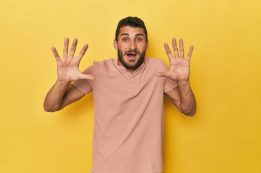 Sarı arka plandaki İspanyol genç adam hoş bir sürpriz alıyor, heyecanlı ve el kaldırıyor..