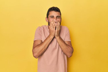 Sarı arka plandaki genç İspanyol bir adam bir şeye gülüyor, elleriyle ağzını kapatıyor..