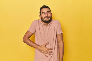 Sarı arka plandaki genç İspanyol adam karnına dokunuyor, nazikçe gülümsüyor, yemek yiyor ve tatmin oluyor..