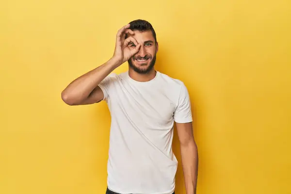 Young Hispanic man on yellow background excited keeping ok gesture on eye.