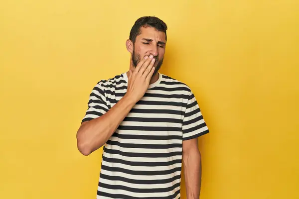 Young Hispanic man on yellow background yawning showing a tired gesture covering mouth with hand.