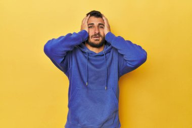 Sarı arka plandaki genç İspanyol adam mutlu bir şekilde ellerini başının üstünde tutarak gülüyor. Mutluluk kavramı.