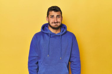 Sarı arka plandaki genç İspanyol adam yanakları siliyor, yorgun bir ifadesi var. Yüz ifadesi kavramı.