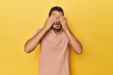Sarı arka plandaki genç İspanyol adam elleriyle gözlerini kapatmaktan korkuyor..
