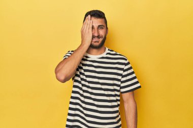 Sarı arka plandaki genç İspanyol, yüzünün yarısını avuç içiyle kaplayarak eğleniyor..