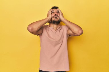 Sarı arka plandaki genç İspanyol adam mutlu bir şekilde ellerini başının üstünde tutarak gülüyor. Mutluluk kavramı.