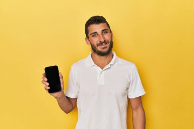 Genç İspanyol adam telefon ekranını mutlu, güler yüzlü ve neşeli gösteriyor..