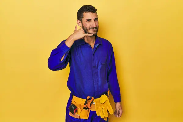 青いジャンプスーツの若いヒスパニックの男 青いジャンプスーツの男 指で携帯電話の通話ジェスチャーをショー — ストック写真