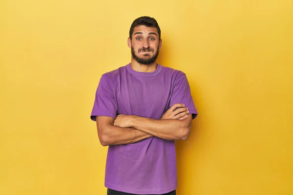 Young Hispanic man on yellow background blows cheeks, has tired expression. Facial expression concept.