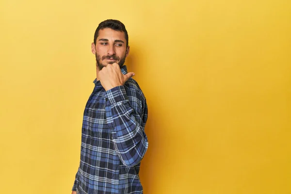 Young Hispanic Man Yellow Background Points Thumb Finger Away Laughing Royalty Free Stock Photos