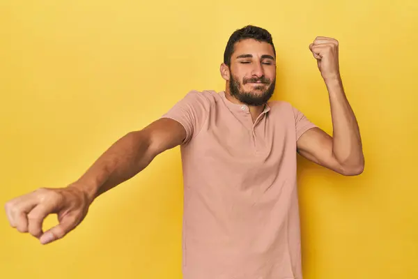 年轻的有黄色背景的西班牙男人庆祝一个特殊的日子 精力充沛地跳起来 举起胳膊 图库图片